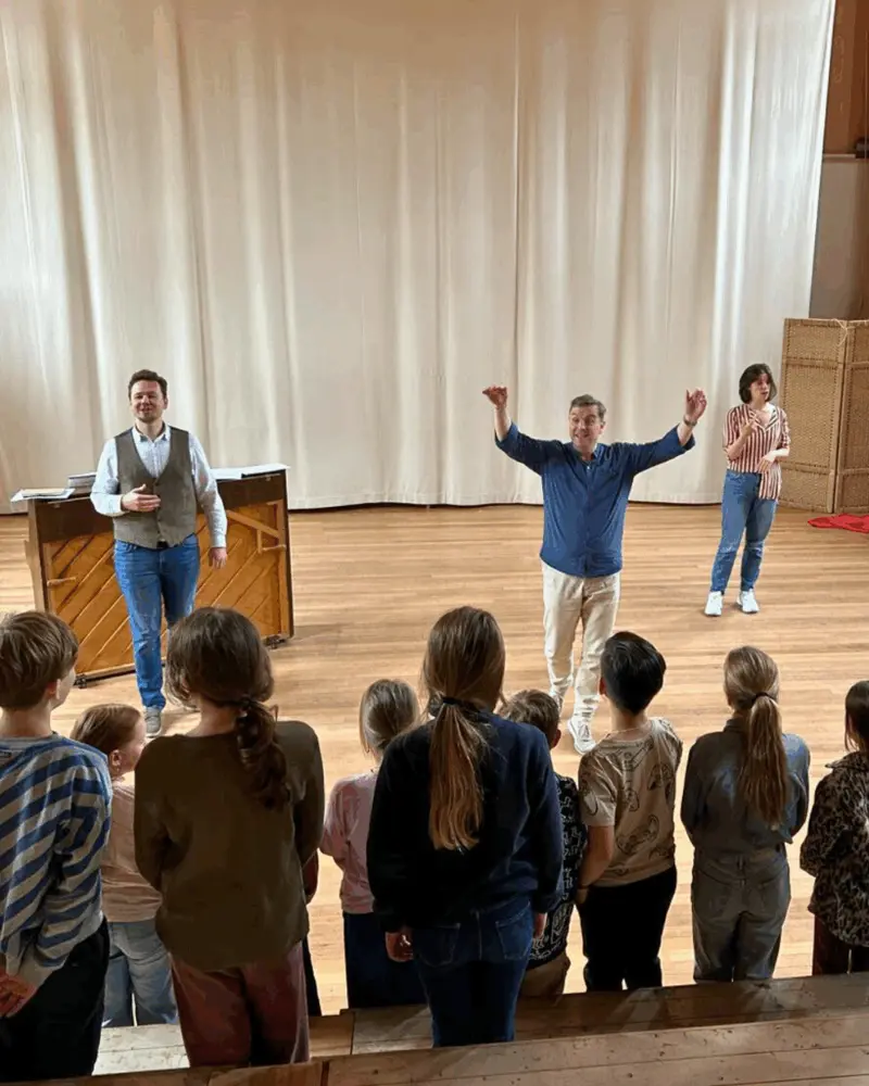 IVC singers leading a vocal exercise with primary-school children on a hall stage